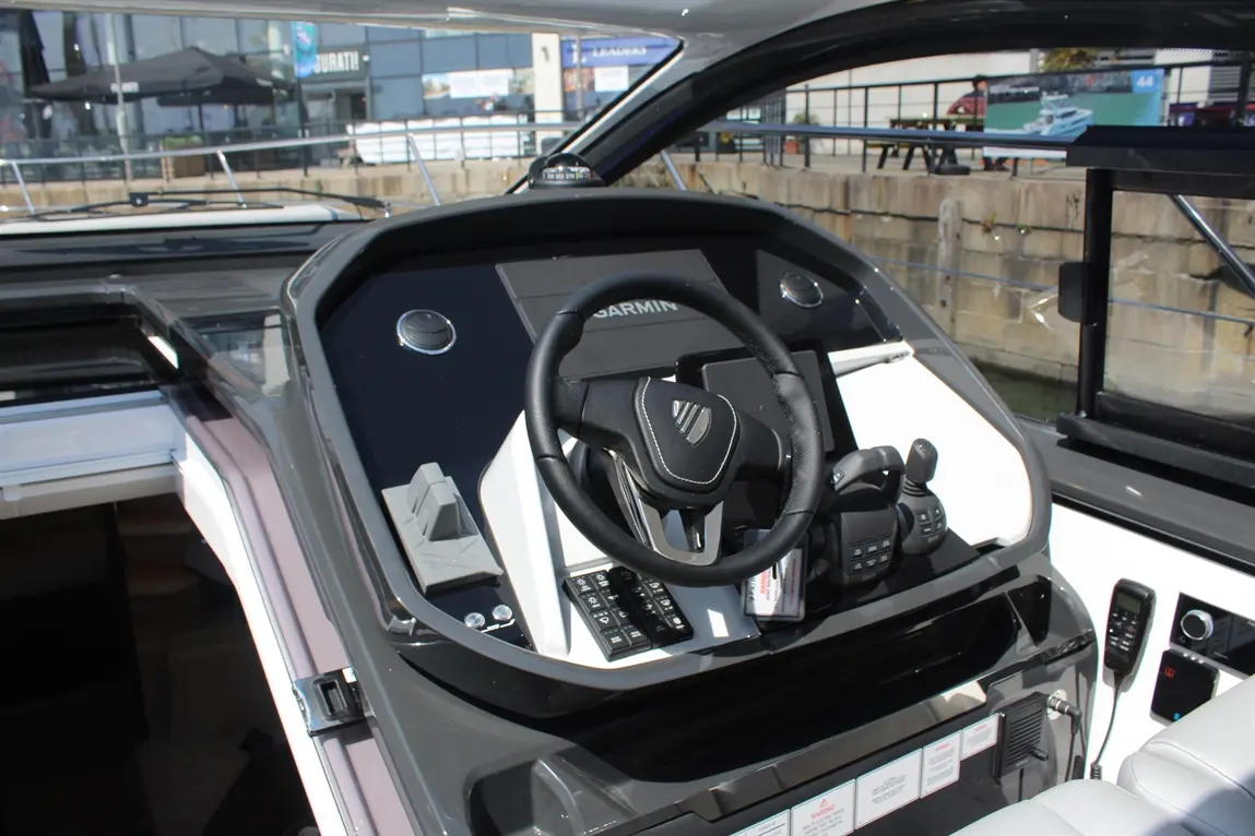 Boat cockpit with Garmin display, steering wheel, controls, and a sunlit marina in the background. Modern marine design.